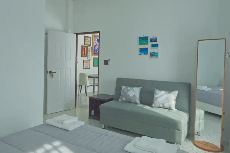 Bright guest bedroom at Baan Bahng Can Do homestay in Nong Thale, Krabi, with sofa bed, full-length mirror, Krabi photo prints, and open door to shared living area