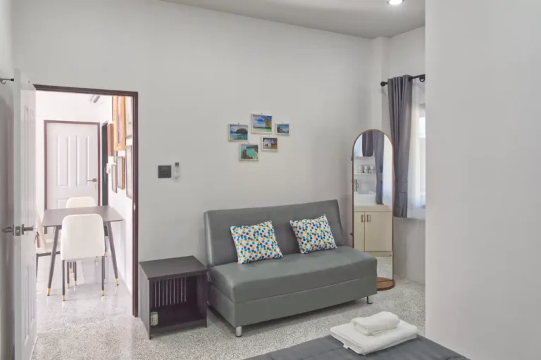 Guest bedroom at Baan Bahng Can Do Krabi homestay showing sofa bed, full-length mirror, Krabi landscape prints, and glimpse of private bathroom with vanity unit