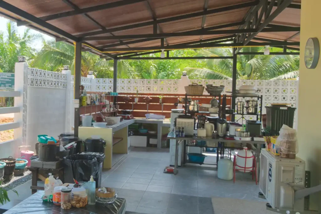 Outdoor Thai cooking kitchen at Baan Bahng Can Do Krabi homestay, fully equipped with prep benches, cooking equipment, and palm tree garden backdrop