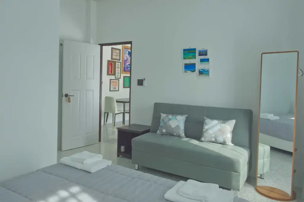 Bright guest bedroom at Baan Bahng Can Do homestay in Nong Thale, Krabi, with sofa bed, full-length mirror, Krabi photo prints, and open door to shared living area
