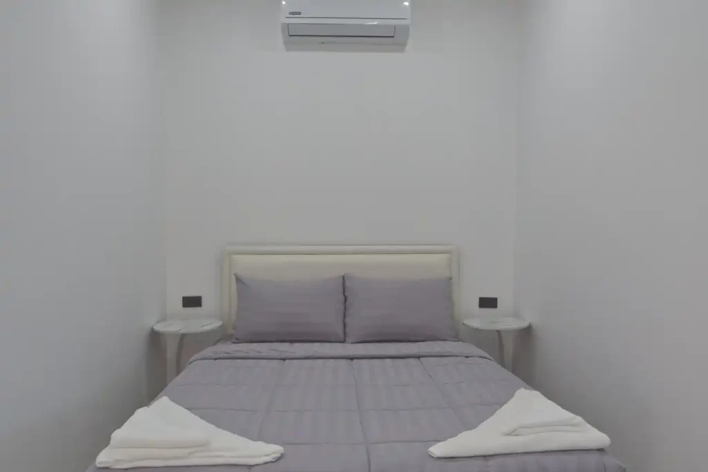 Queen bed with grey bedding, twin bedside tables, and air conditioning in Bedroom 2 at Baan Bahng Can Do Krabi homestay, with fresh towels laid out