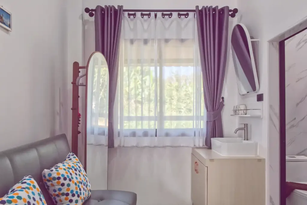 Bedroom 4 at Baan Bahng Can Do Krabi homestay with large garden-view window, distinctive purple curtains, full-length mirror, sofa bed, and en-suite vanity unit